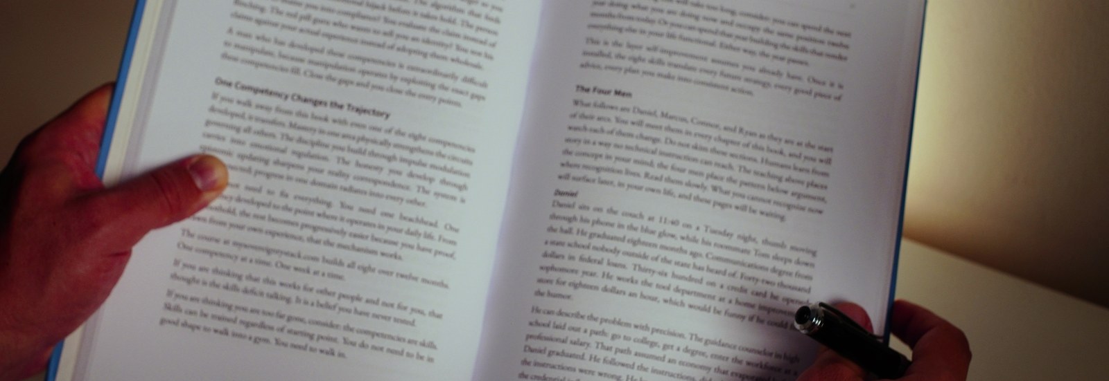 A pair of hands with an open book and a pen, on a plain ground.